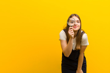 young pretty woman  with a magnifying glass against orange background