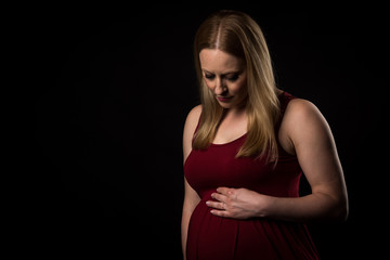 Pregnant woman in red dress holding belly on black background.