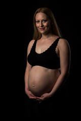Pregnant woman in black underwear holding belly on black background.