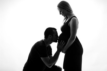 Silhouette portrait of Husband man kissing pregnant woman belly.