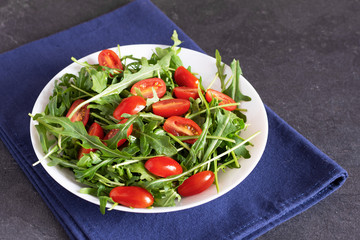 Salad with fresh green arugula and tomato cherry in a white ceramic bowl.