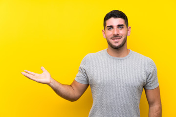 Young handsome man over isolated yellow background holding copyspace imaginary on the palm