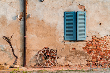 Fototapeta na wymiar Old brick Italian house with the wooden wheel, blue window and wooden shutters
