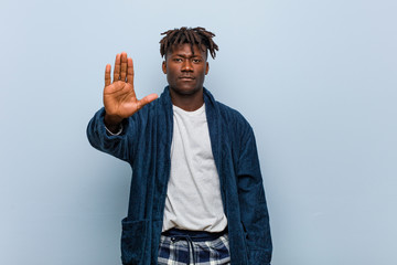 Young african black man wearing pajama standing with outstretched hand showing stop sign,...
