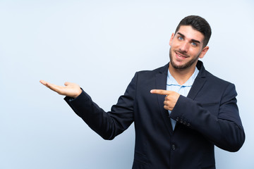 Handsome man over isolated blue background holding copyspace imaginary on the palm to insert an ad