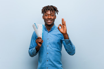 Young rasta black man holding an air tickets cheerful and confident showing ok gesture.