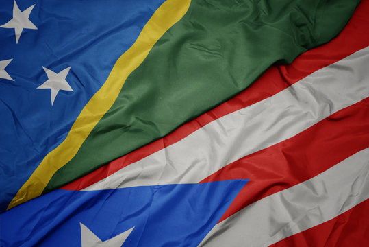 waving colorful flag of puerto rico and national flag of Solomon Islands .