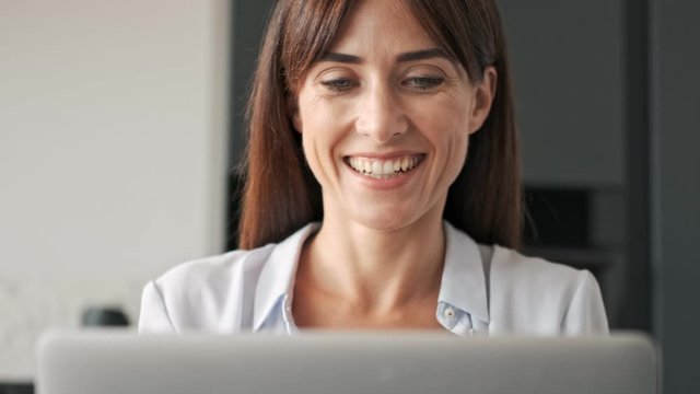 Charming cute young business woman smiling and working on laptop while sitting at the table