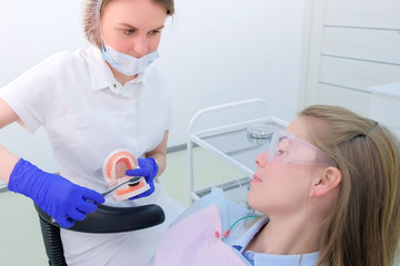 Naklejka premium Dental oral hygiene. Dentist shows patient on jaw model how to clean teeth with toothbrush properly. Dental hygienist teach young woman to brush teeth in stomatology clinic.
