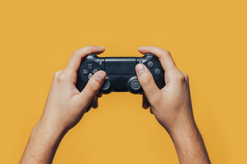 man gamer hands holding black gamepad on yellow background. © Anastassiya 