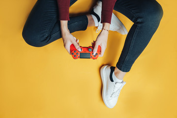 Young thin woman playing with red gamepad, sitting on yellow background. flat lay. © Anastassiya 