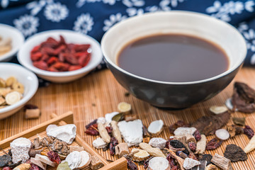 Various Chinese herbal medicines and a bowl of Chinese herbal medicine soup scattered on bamboo mats