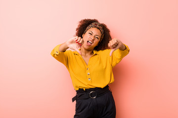 Young african american woman against a pink background showing thumb down and expressing dislike.