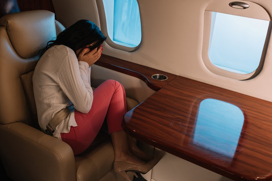 frightened woman with airsickness covering face while sitting in private jet