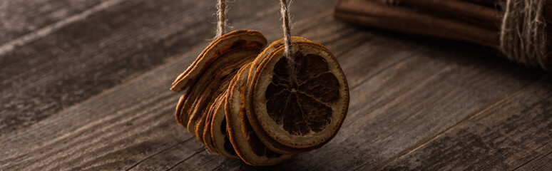 dried orange slices on thread and cinnamon on wooden background, panoramic shot
