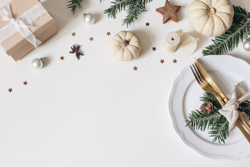 Traditional Christmas table place setting. Golden cutlery, porcelain plate, fir tree branches, gift box, pine cones and white pumkins. Christmas baubles decoration. Holidays background. Flat lay, top.