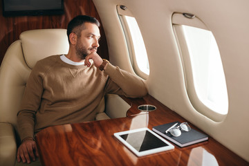 handsome bearded man looking at airplane window in first class of private jet