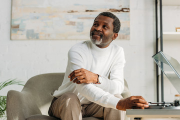 smiling african american man looking away while listening music on record player