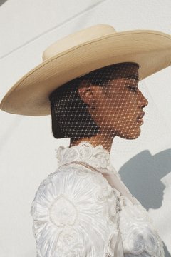 Close up of model wearing straw hat with veil and formal dress