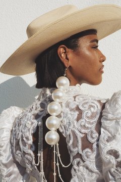 Model in formal dress with oversize pearl earring  and straw hat