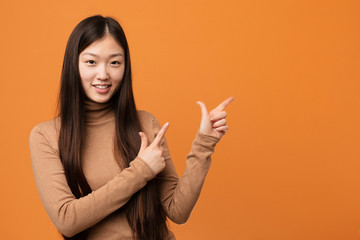 Young pretty chinese woman pointing with forefingers to a copy space, expressing excitement and...