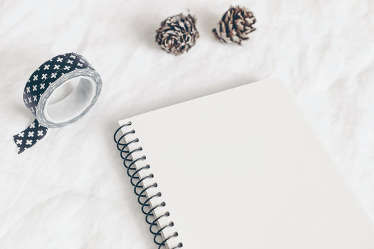 Christmas styled stock photo. Notebook, diary mockup. Still life with washi tape, larch cones on white linen background. Winter startionery. Image for blog or social media, selective focus.