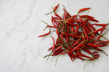 View from above of a pile of bright red Thai bird chiles on a white marble cutting board with copy space