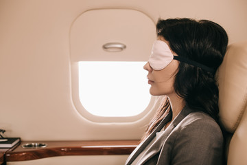 Fototapeta na wymiar side view of businesswoman in sleeping mask sitting in private jet