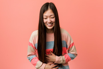 Young cool chinese woman laughs happily and has fun keeping hands on stomach.