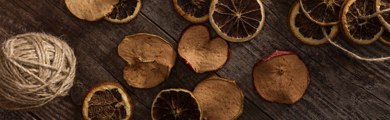 top view of dried citrus and apple slices near ball of thread on wooden surface, panoramic shot