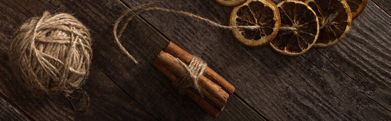 top view of dried citrus slices on rope near cinnamon on wooden surface, panoramic shot
