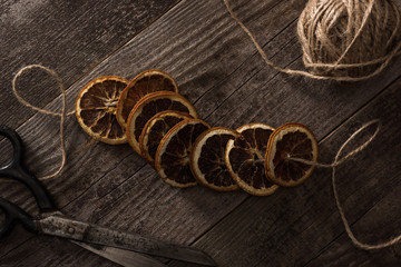 top view of thread, scissors and dried citrus slices on wooden background