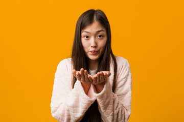 Young chinese woman in pajama folding lips and holding palms to send air kiss.