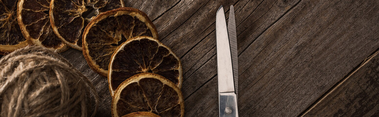 top view of thread, scissors and dried citrus slices on wooden background, panoramic shot