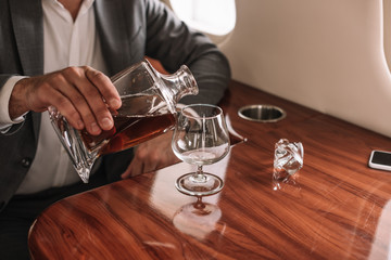 cropped view of businessman pouring cognac into glass in private jet