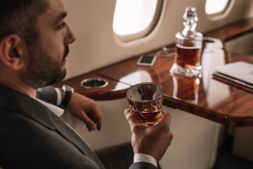 selective focus of bearded man holding glass with whiskey in private jet