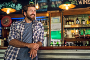 Smiling thoughtful man leaning against bar counter