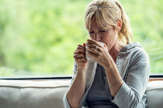 Mature woman having coffee while sitting on sofa at home