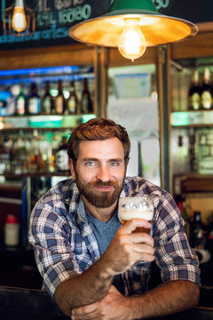 Smiling man holding a beer glass while leaning at bar counter