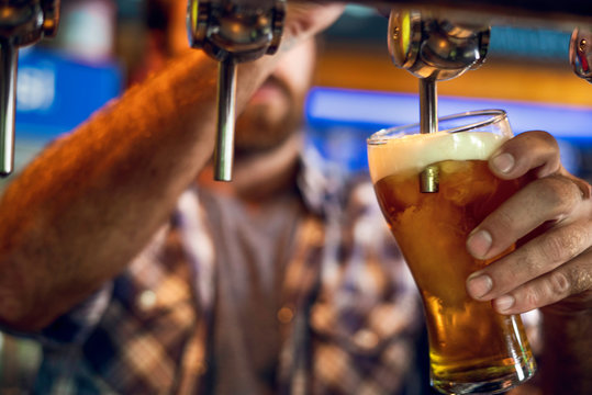 Close-up Of Man Drawing Beer From Tap Into A Glass In The Bar