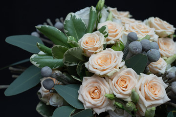Beautiful wedding bouquet of bushy cream rose, eucalyptus, Brunei, Pittosporum and Lisianthus on a black background.