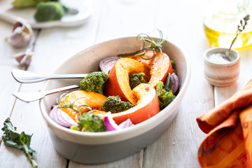 Traditional autumn pumpkin dishes. Grilled roasted pumpkin with spices, olive oil, herbs, broccoli and onions. On a baking sheet, on a rustic wooden white background.