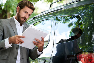Car salesman reading documents while standing by car