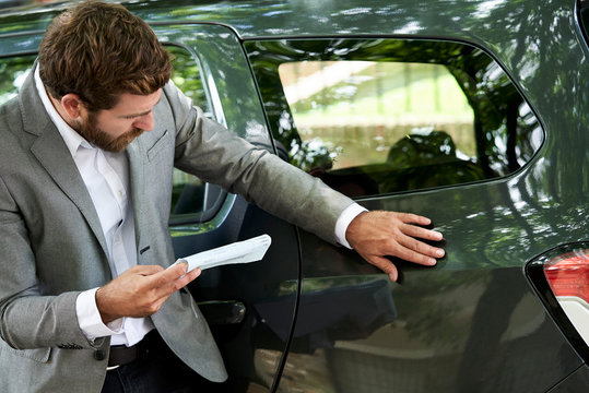 Car salesman with documents examining a car