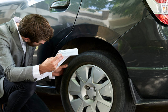 Car salesman examining car tyre while holding documents