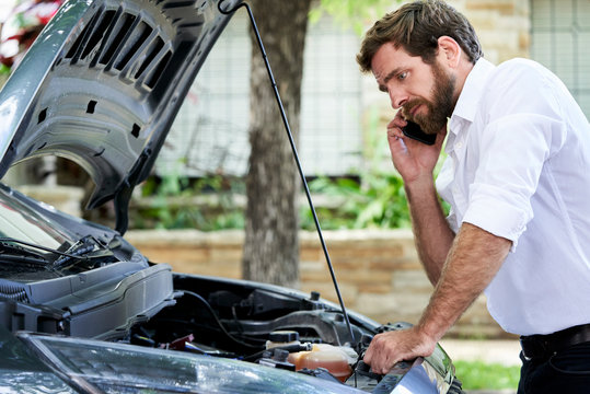 Man talking on mobile phone while standing by broken car