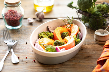 Traditional autumn pumpkin dishes. Grilled roasted pumpkin with spices, olive oil, herbs, broccoli and onions. On a baking sheet, on a rustic wooden white background.