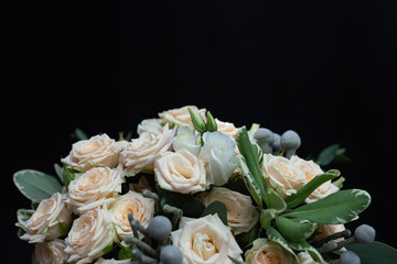 Beautiful wedding bouquet of bushy cream rose, eucalyptus, Brunei, Pittosporum and Lisianthus on a black background.