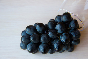 Bunches of fresh ripe red grapes and glass for wine on a white wooden background, top view, copy space. Table setting. Beautiful background with a branch of blue grapes. Red wine grapes.