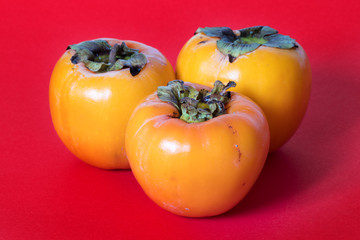 three persimmons on red background